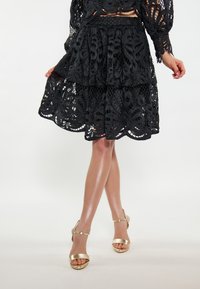 Gonna di pizzo nero con un design a strati e intricati motivi floreali. Abbinata a sandali con tacco alto dorati con fascette sottili.