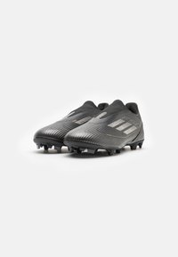 Botas de fútbol negras con un material sintético texturizado, que presentan rayas geométricas, un collar ajustado y clavos negros para tracción.