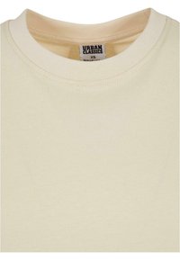 Beige bomull T-shirt med rund hals. Slät textur, med en sömdesign vid halsen. Etiketten säger "URBAN CLASSICS", storlek XS.
