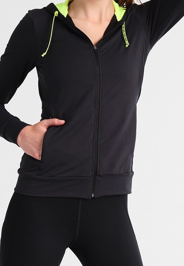 Sweat à zip noir avec un intérieur vert fluo et des accents de cordon. Dispose de manches longues et d'une poche avant. Tissu lisse et extensible.