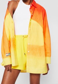 Overhemd met knopen met een verloop van oranje naar geel, gecombineerd met gele shorts met koordsluiting. Katoenen textuur, ontspannen pasvorm en zichtbare labeldetails.