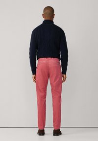 Marineblauwe kabelgebreide trui, roze corduroy broek met achterzakken en donkerbruine schoenen. Eenvoudig, getailleerd ontwerp, gladde textuur.