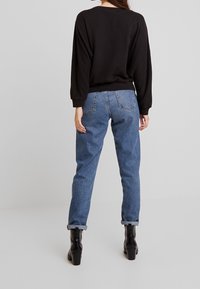 Sudadera negra con hombros caídos y puños de canalé, combinada con jeans de pierna recta de color azul claro, con dobladillos enrollados, y botas de plataforma negras.