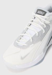 Białe i srebrne sneakersy Nike z błyszczącymi detalami, białymi sznurówkami oraz widocznymi logo Nike na języku i boku.