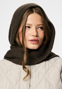 Brun ribbet strikket tørklæde brugt som hætte, der giver en hyggelig tekstur. Parret med en let quiltet jakke i en neutral farve.