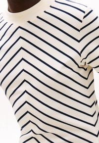 Kortärmad skjorta i creamfärgad bomull med marino-blå diagonala ränder. Har en rund halsringning och subtila sömdetaljer.