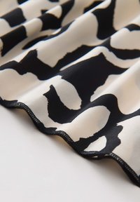 Tessuto nero e crema con un grande motivo astratto, superficie liscia con una finitura leggermente lucida e un bordo cucito in nero.