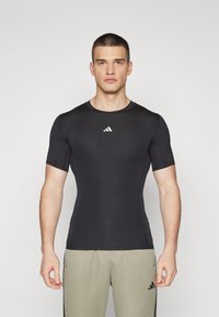 Sort sports t-shirt med korte ærmer, tætsiddende design og hvidt logo på brystet, lavet af glat, strækbart stof.