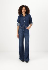 Denim jumpsuit med innsvingt midje, knappestolpe foran og puffede ermer i mørk blå. Har vide ben og lyse denimdetaljer.