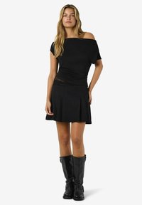 Črna majica brez naramnic s prilegajočim korzetom in čipkastim dodatkom. Usklajena s črno plisirano mini krilo in črnimi usnjenimi škornji do kolen.