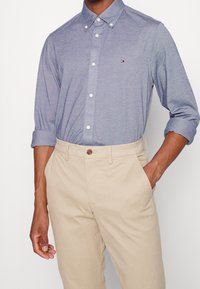 Camisa azul claro de algodón con botones, con cuello y mangas remangadas. Combinada con pantalones beige con cierre de botón.