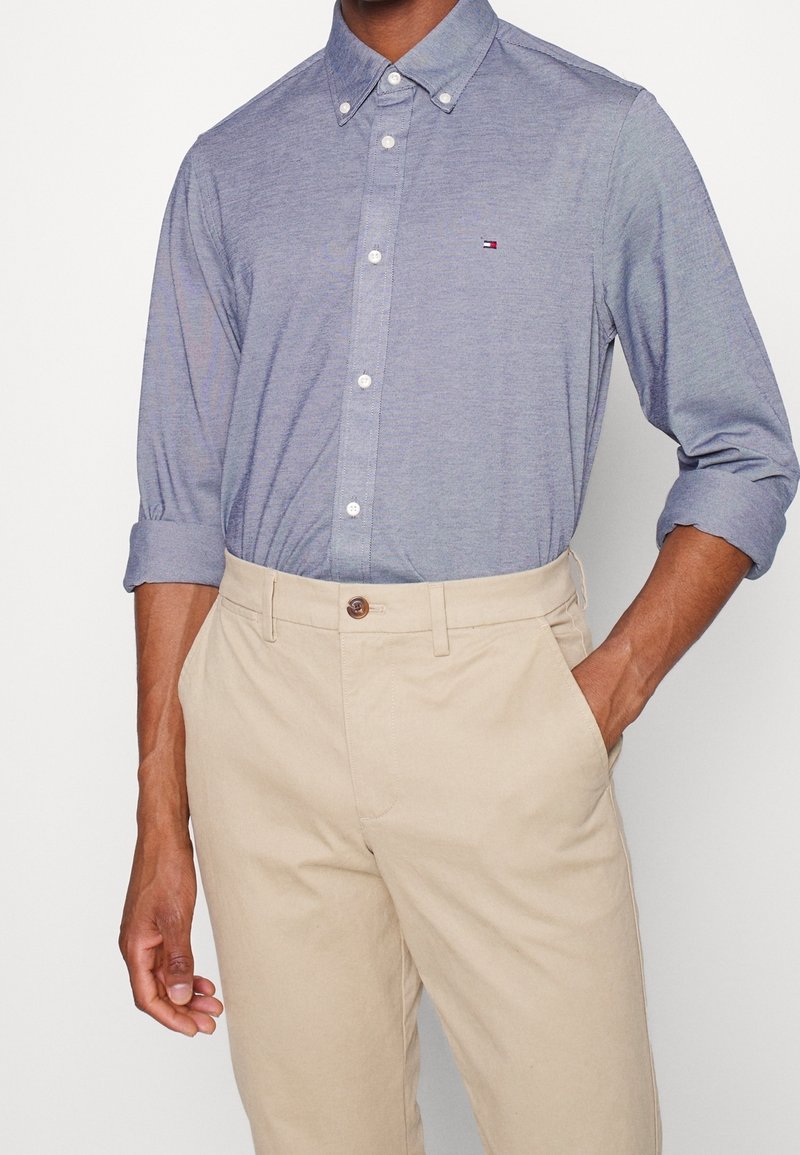 Camisa azul claro de algodón con botones, con cuello y mangas remangadas. Combinada con pantalones beige con cierre de botón.