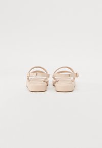 Nude-colored sandals with a flat sole and dual adjustable straps, featuring a smooth material and a simple buckle detail.