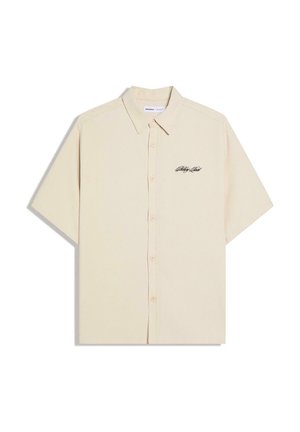 Beżowa krótka koszula na guziki z kołnierzykiem i małym czarnym logo w formie napisu na lewej piersi.