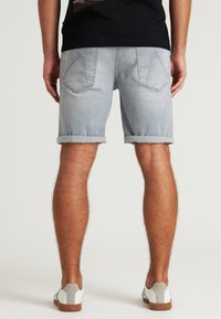 Pantalones cortos de mezclilla azul claro con dobladillos enrollados, que cuentan con dos bolsillos traseros y una textura suave. Combinados con zapatillas blancas y grises.