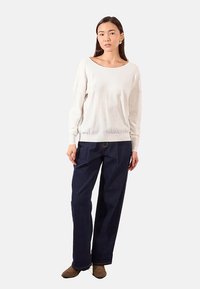 Maglione leggero in crema con scollatura ampia abbinato a pantaloni a gamba larga blu scuro. Il maglione ha una texture morbida, mentre i pantaloni sono in denim.