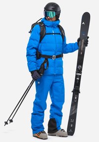 Blaue isolierte Skijacke und -hose, schwarzer Helm, verspiegelt Goggles, hält schwarz Ski und Skistock, mit technischem Design, verstellbaren Riemen.