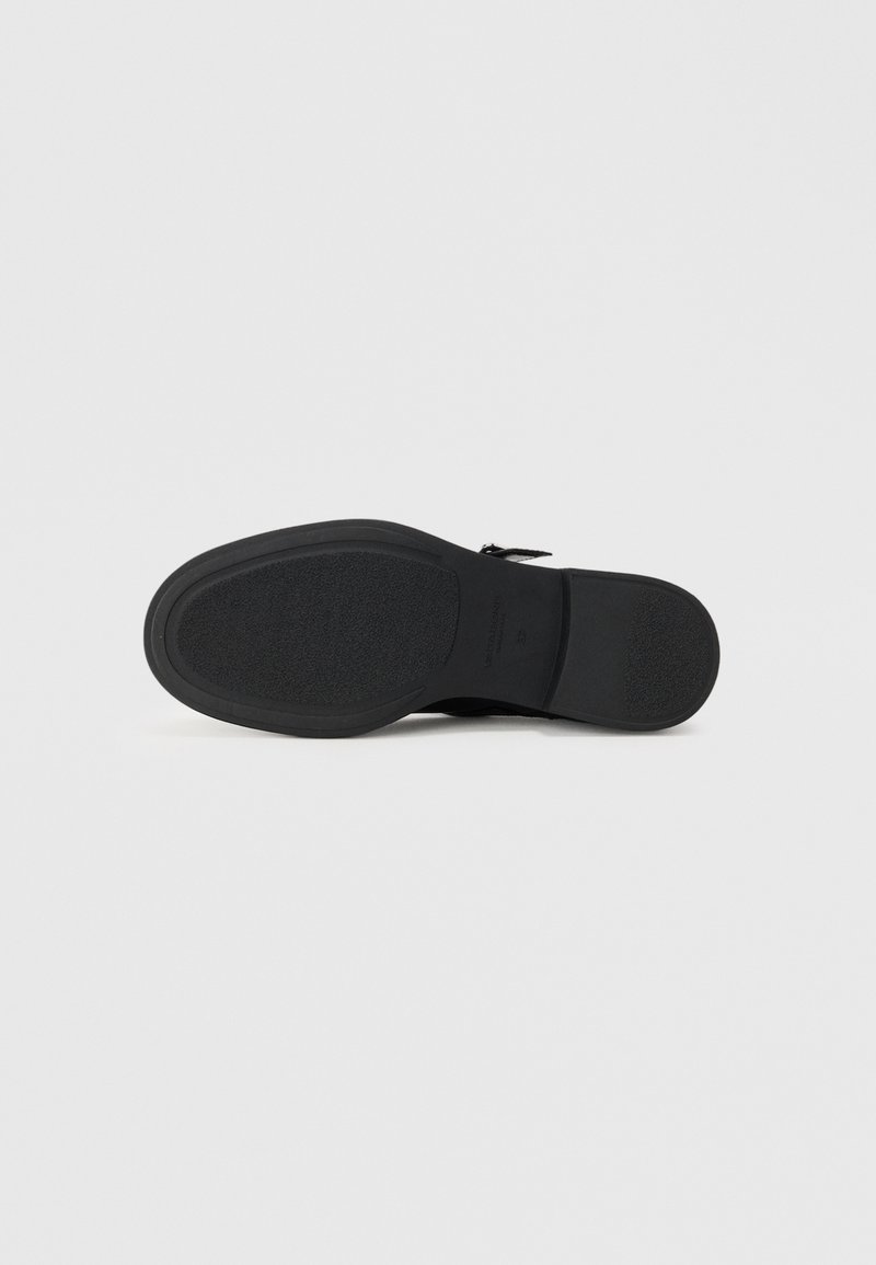 Semelle de chaussure noire avec une poignée en caoutchouc texturé et des bords lisses. Présente un branding subtil et un design élégant pour la stabilité et l'adhérence.