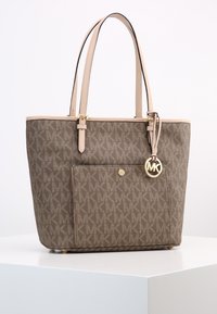 Sac fourre-tout en toile brun avec des poignées en simili cuir clair, poche avant, logo décoratif doré et motif de monogramme subtil.