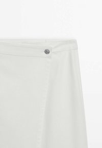 Jupe portefeuille blanche avec une fermeture à bouton-pression métallique à la taille, texture lisse et coutures nettes sur fond uni.