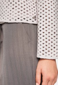 Hellgraue, strukturierte Jacke mit einem perforierten Design, ausgestattet mit einem silbernen Knopf. Kombiniert mit grauen Hosen im Fischgrätmuster.