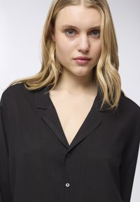 Camicia nera a maniche lunghe con un tessuto morbido e leggero. Presenta un colletto e un scollo a V. Texture liscia e vestibilità comoda.