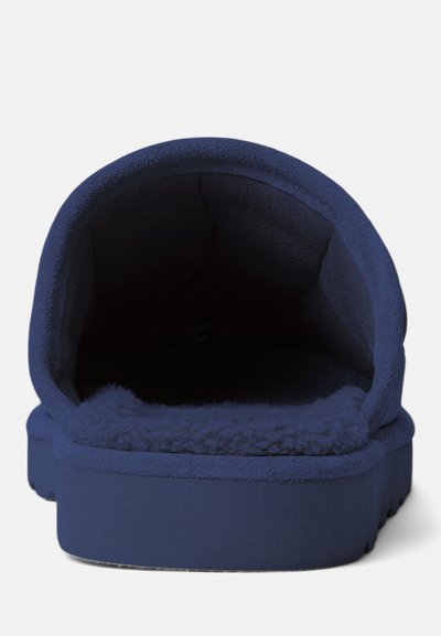 Marineblauwe slipper met een zachte, donzige binnenkant en een afgeronde, gevoerde opening. Beschikt over een platte zool en een gladde buitenkant.