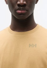T-shirt en coton beige avec col rond, manches courtes et logo "HH" ton sur ton sur le côté gauche de la poitrine. Texture lisse avec peu de détails.