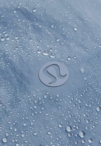 Vesipitävä sininen kangas, jossa on sileä pinta, ja siinä on lukuisia vesipisaroita sekä pyöreä logo alhaalla keskellä.