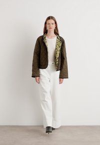 Veste matelassée marron avec doublure imprimée verte, associée à un pantalon blanc à jambes larges et des bottines grises. Texture lisse, design moderne.
