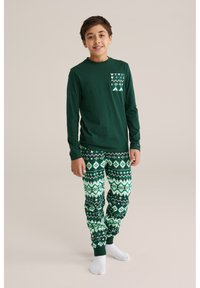 Cămașă verde cu mânecă lungă, având un buzunar patern și pantaloni de pijama verzi asortați, cu un imprimeu geometric în nuanțe variate de verde.