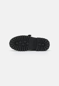 Black rubber shoe sole with deep treads, featuring rectangular and cross patterns. Flat design with a textured finish for grip.