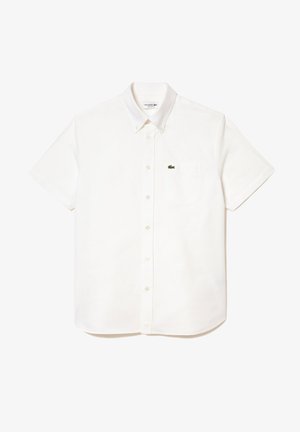 Lühikeste varrukatega valge puuvillane särk nööpidega kaelusega, millel on rinna tasku ja väike roheline krokodillilogoga vasakul küljel.