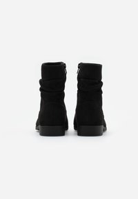 Bottines en suède noir avec un design décontracté, dotées d'une fermeture éclair sur un côté et d'un petit talon carré pour plus de stabilité.