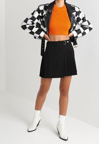 Skórzana kurtka w czarno-białą kratę, pomarańczowy prążkowany krótki top, czarna plisowana spódnica i białe botki z noskiem w szpic.