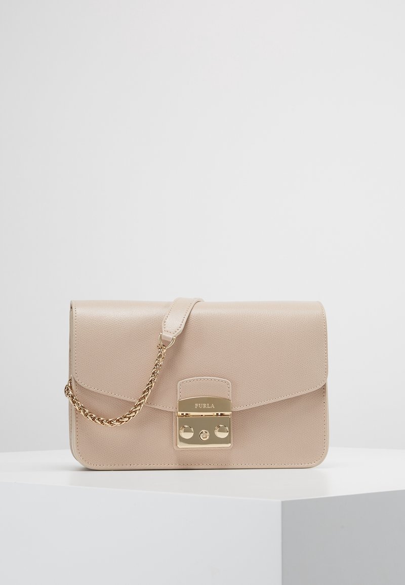 Beige leather crossbody bag with gold chain strap and gold clasp engraved with "Furla" on white surface and gray background.