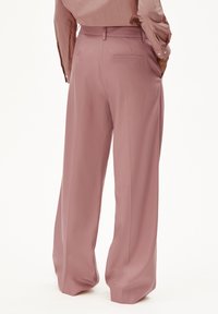 Rosa weit geschnittene Hose aus glattem Stoff, mit einem Bund mit Gürtelschlaufen und einer einzelnen Gesäßtasche. Die Textur ist weich und strukturiert.
