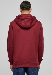 Sudadera burdeos con una gran capucha adjunta, hecha de una tela suave, con mangas largas y un corte a la altura de la cintura.