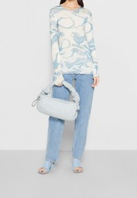 Top azzurro chiaro a maniche lunghe con motivi astratti bianchi, abbinato a jeans dal lavaggio chiaro e una borsa blu chiaro morbida con manico annodato.