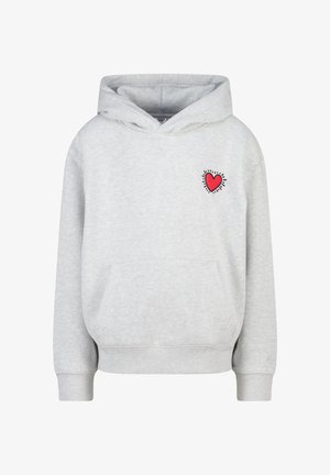 Sudadera gris con un gráfico de corazón en el pecho, combinada con vaqueros anchos de pierna azul claro con franjas laterales y zapatillas blancas.