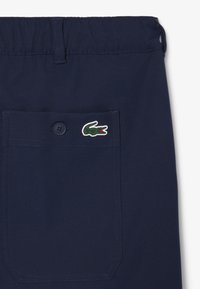 Shorts bleu marine en tissu léger, dotés d'une fermeture à bouton et d'un logo en patch. Comprend une poche arrière avec des coutures visibles.