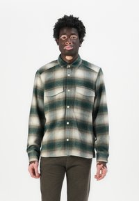 Groen en crèmekleurig geruite shirt met twee borstzakken, knoopsluiting en katoen stof. Gestyled met donkere broeken.