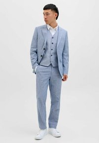 Costum trei piese de culoare albastru deschis, realizat dintr-un material texturat, care include un sacou ajustat, o vestă cu nasturi și pantaloni asortați. Cămașă albă dedesubt.