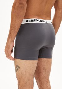 Graue Boxershorts mit einem weißen Bund, der mit "ARMEDANGELS" beschriftet ist. Sie verfügen über eine glatte Textur und ein eng anliegendes Design, mit Kontrastnähten.