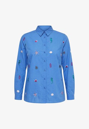 Sininen pitkähihainen nappipaitapusero kauluksella, koristeltu kirjotuilla meriaiheisilla kuvioilla kuten merihevosilla, meritähdillä, simpukoilla ja korallien oksilla.