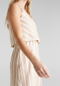 Raidallinen hihaton toppi kermaan ja ruosteenvärisin viivoin, rento istuvuus ja lyhyt malli. Pehmeä materiaali suoralla helmalla.