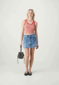 Haut de tank court rayé rouge et blanc, mini-jupe en denim avec un ourlet effiloché, ballerines noires, et un petit sac à cordon noir à motifs.