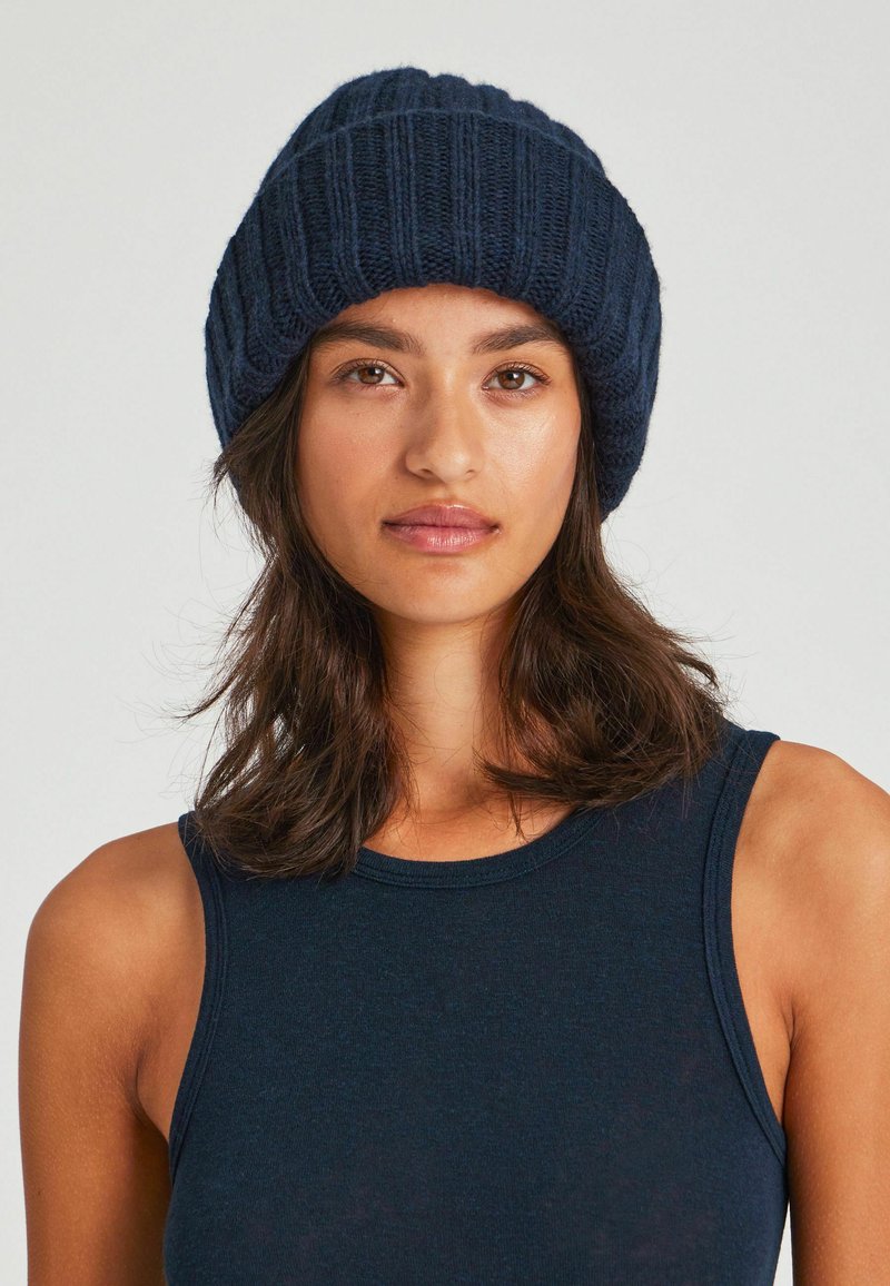 Stickad mössa i mörk marinblått, med ribbat mönster och uppvikt mudd. Mjukt material, elastiskt, utformat för värme i kallt väder.