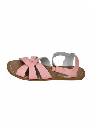 Pink flat sandal with crisscross straps, ankle buckle closure, and brown sole, shown from a side view on a white background.
