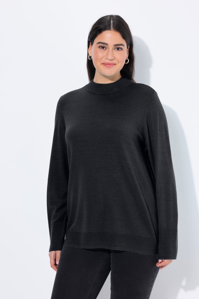 Femme aux cheveux foncés portant des boucles d'oreilles argentées en forme d'anneau et un pull noir à manches longues, debout sur un fond blanc, souriant doucement.